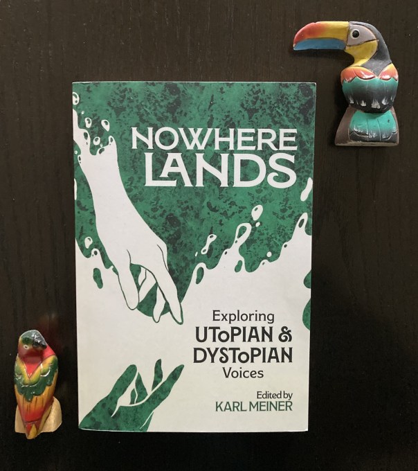 Cover of textbook Nowhere Lands: Exploring Utopian & Dystopian Voices, with green and white hands reaching toward each other. The book is surrounded by two balsa wood bird figurines, one a toucan and one a parrot.