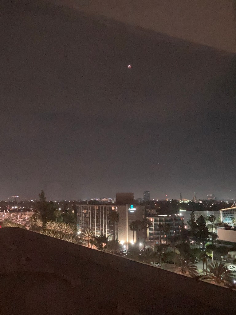 Evening view of Anaheim skyline with partial lunar eclipse high above.