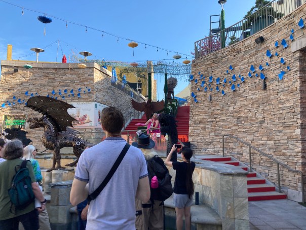 Crowd looking at metal dragon sculptures in front of a stone wall.